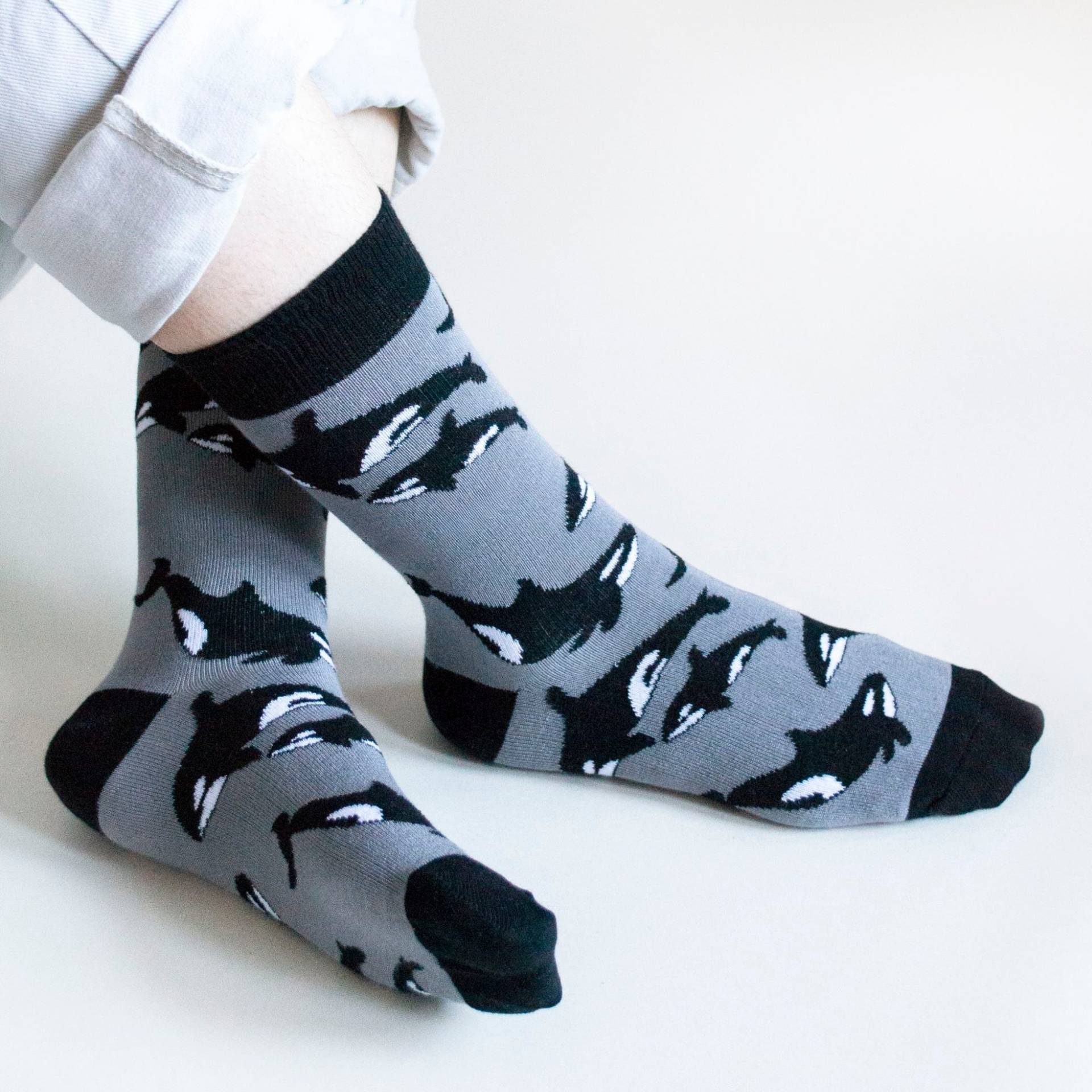 Gray socks with black orca pattern worn by a person on a white background