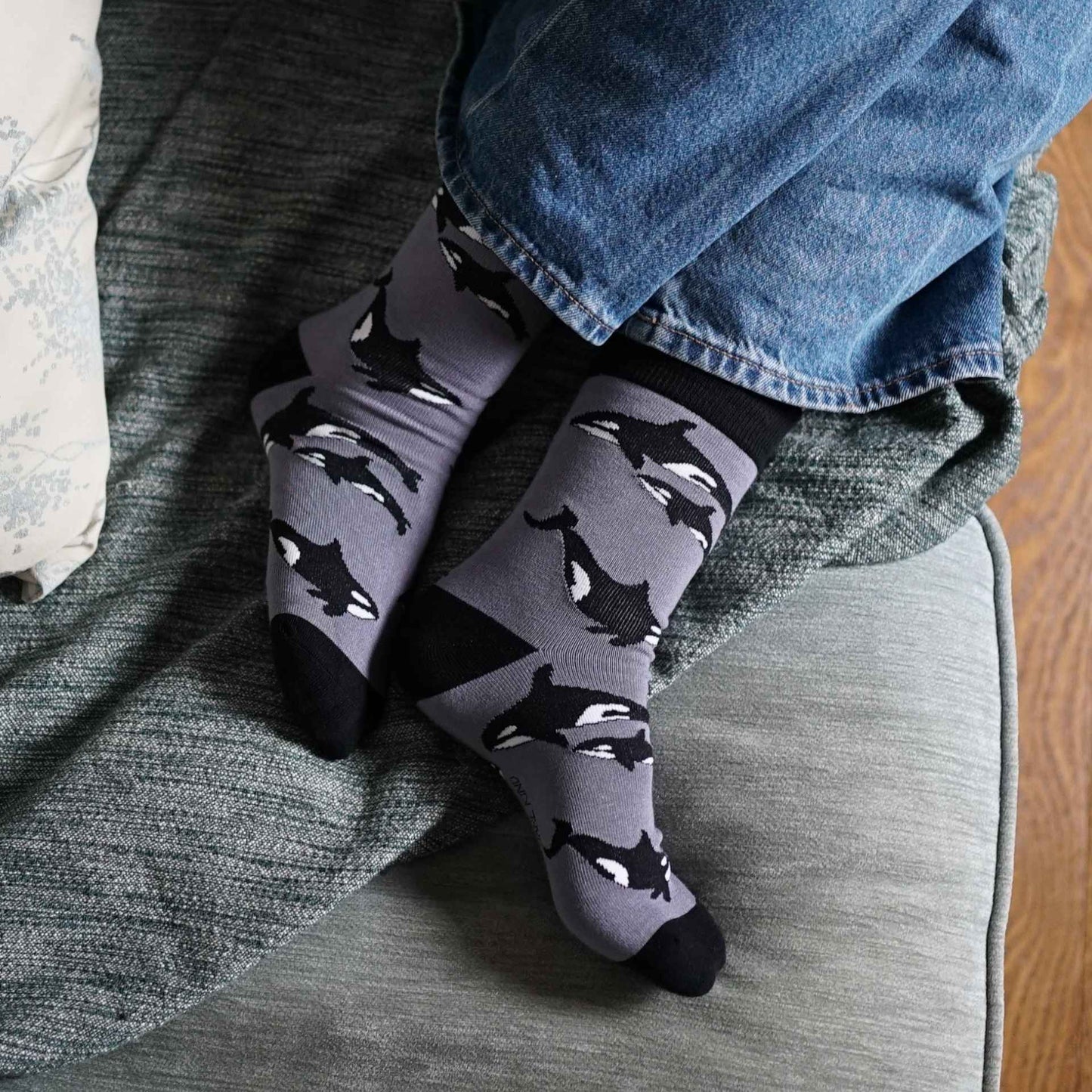 Gray socks with orca pattern worn by a person sitting on a couch.