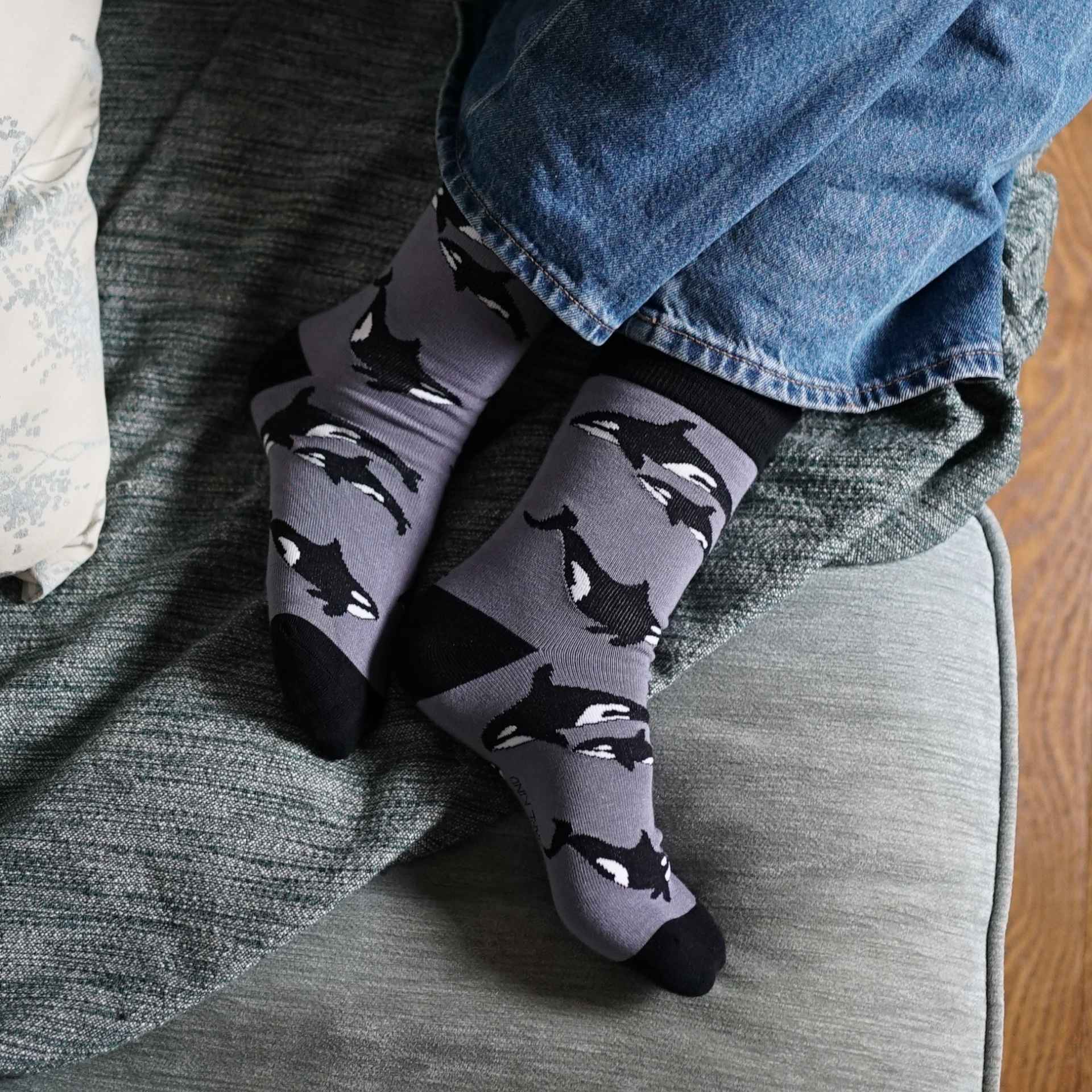 Gray socks with orca pattern worn by a person sitting on a couch.