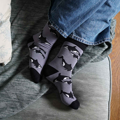 Gray socks with orca pattern worn by a person sitting on a couch.