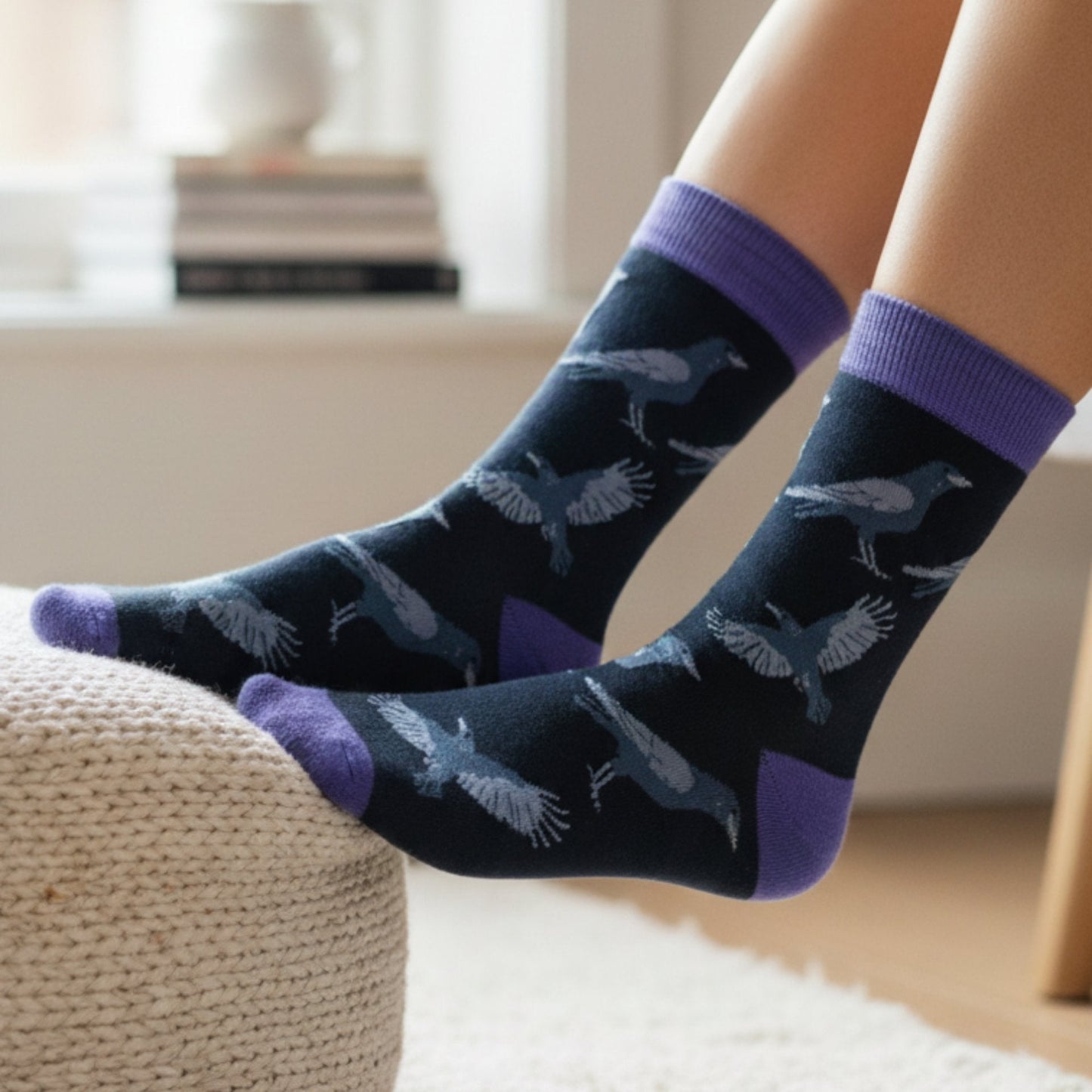 Navy socks with raven pattern and purple accents worn by a person sitting on a couch.